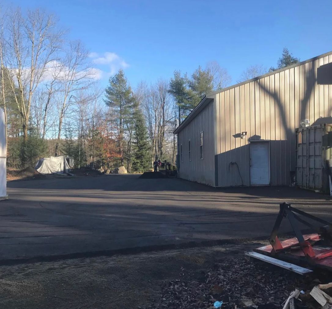 Empty paved lot beside beige industrial buildings under a clear blue sky.