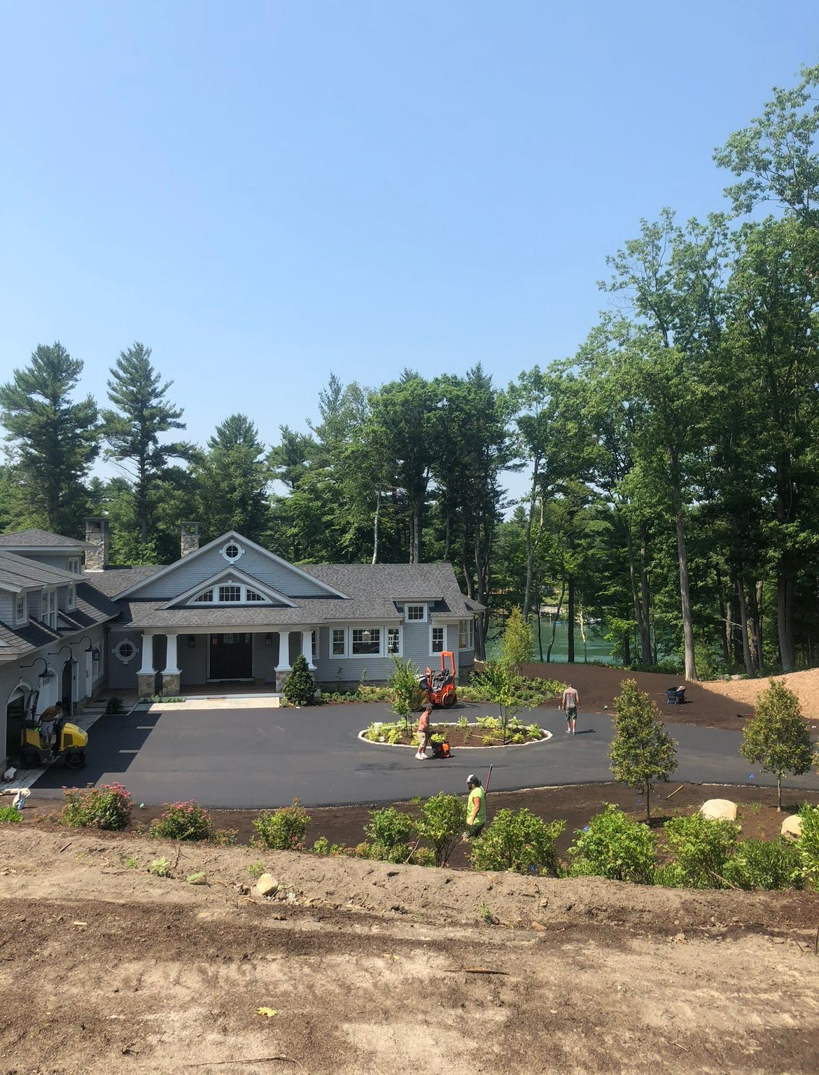 Landscaped house with a driveway, front porch, and flower bed surrounded by tall trees.