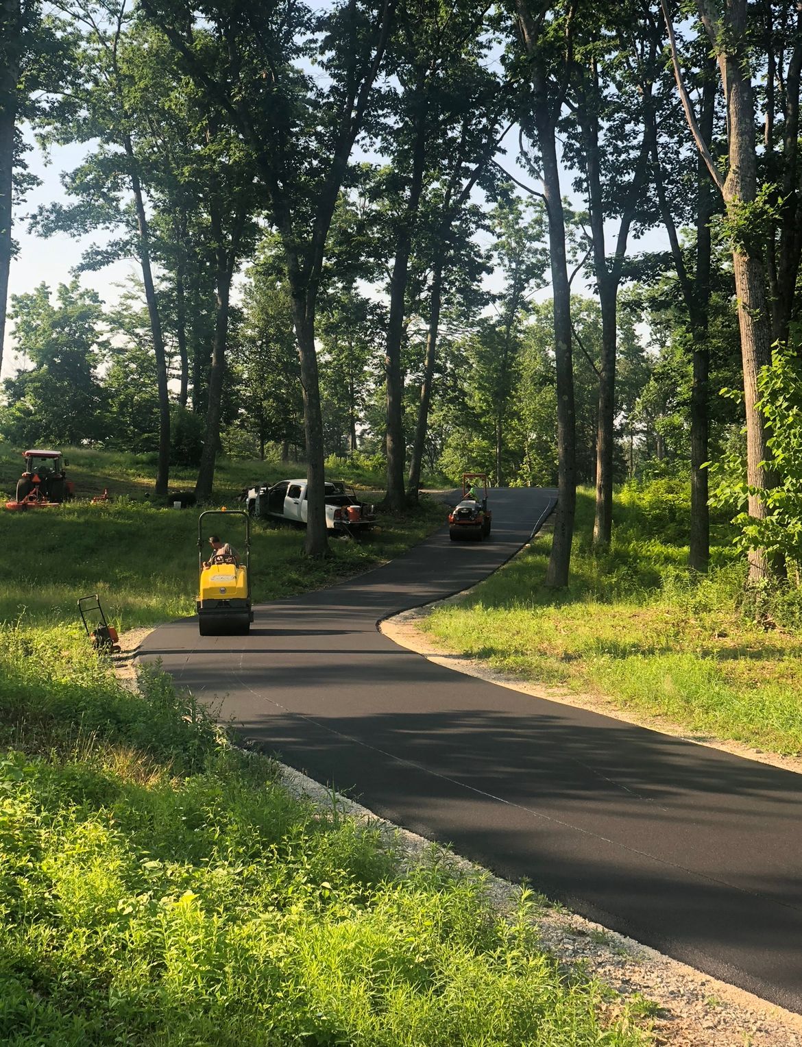 Winding paved path through a wooded park, with a small yellow cart moving away