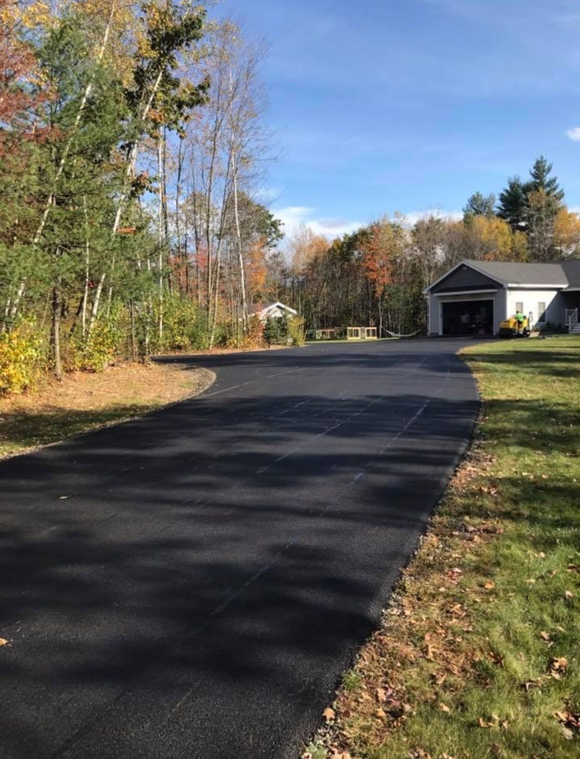 Curved asphalt driveway beside trees and a garage in a quiet suburban neighborhood, with autumn foliage.