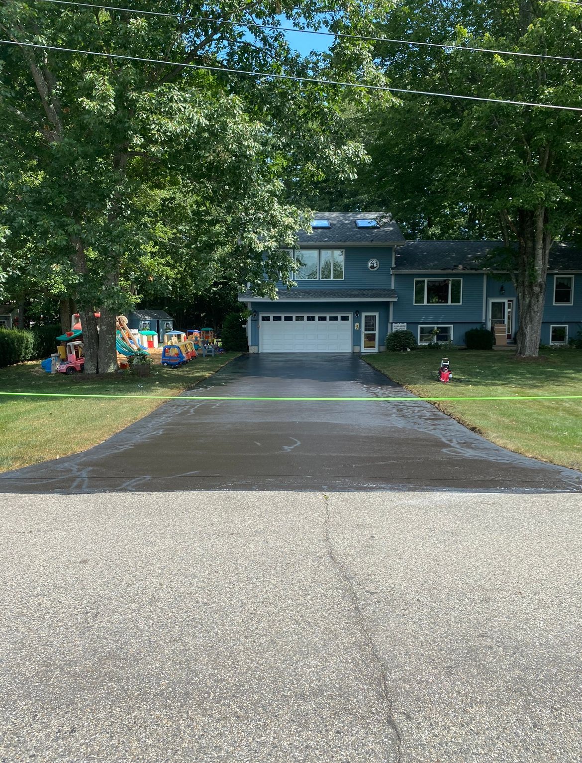 Tree-lined driveway leading to a gray two-story house with a garage and red front door.