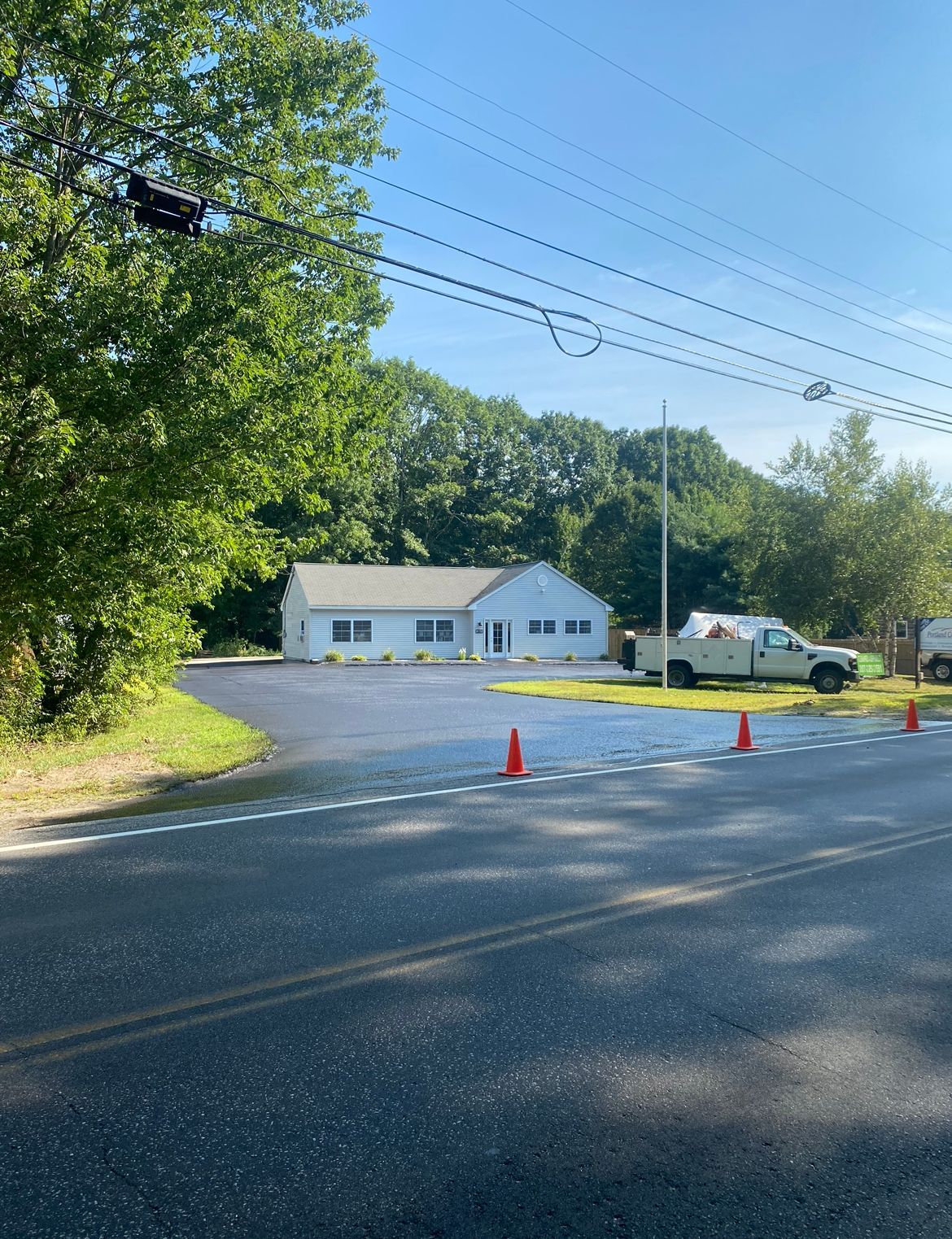 Roadside building with orange cones, parked van, and trees under a clear blue sky