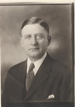 Studio portrait of a man in a dark suit, tie, and pocket square against a plain background