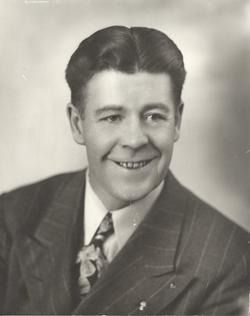 Black-and-white studio portrait of a smiling man in a suit and patterned tie.
