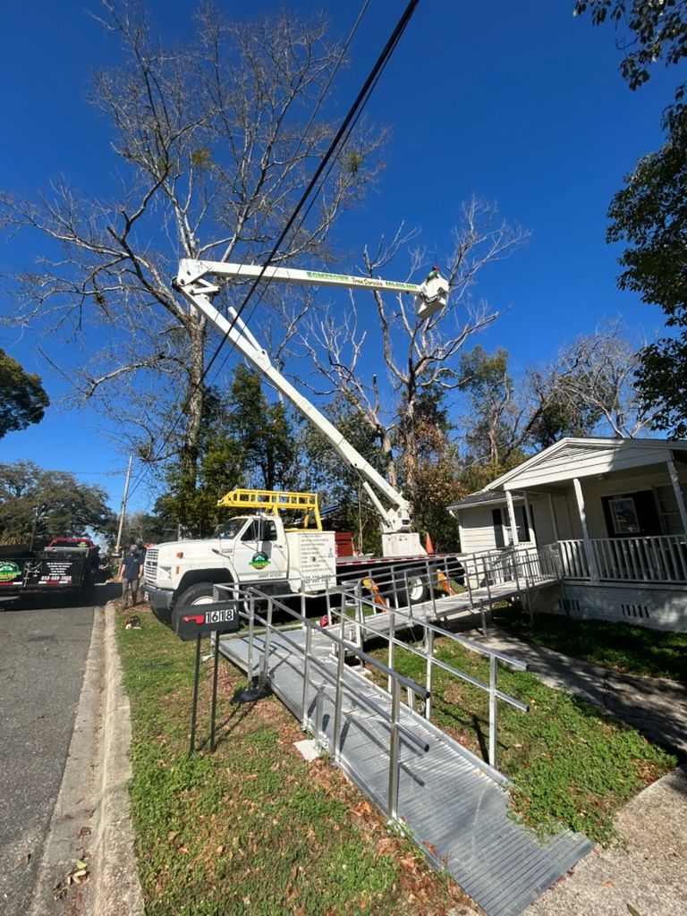 A white utility truck with an extended boom arm parked next to a house with a metal wheelchair ramp on a sunny day.