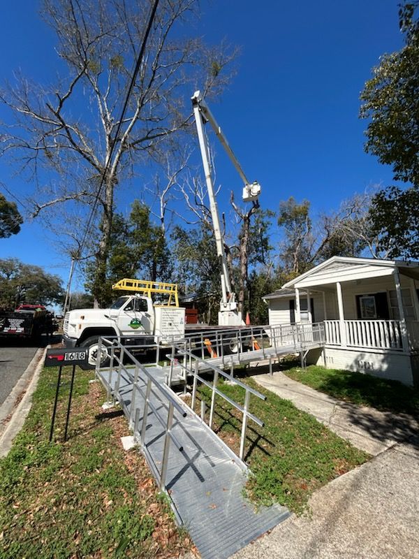 A utility bucket truck parked in a residential yard next to a white house with an aluminum wheelchair ramp.
