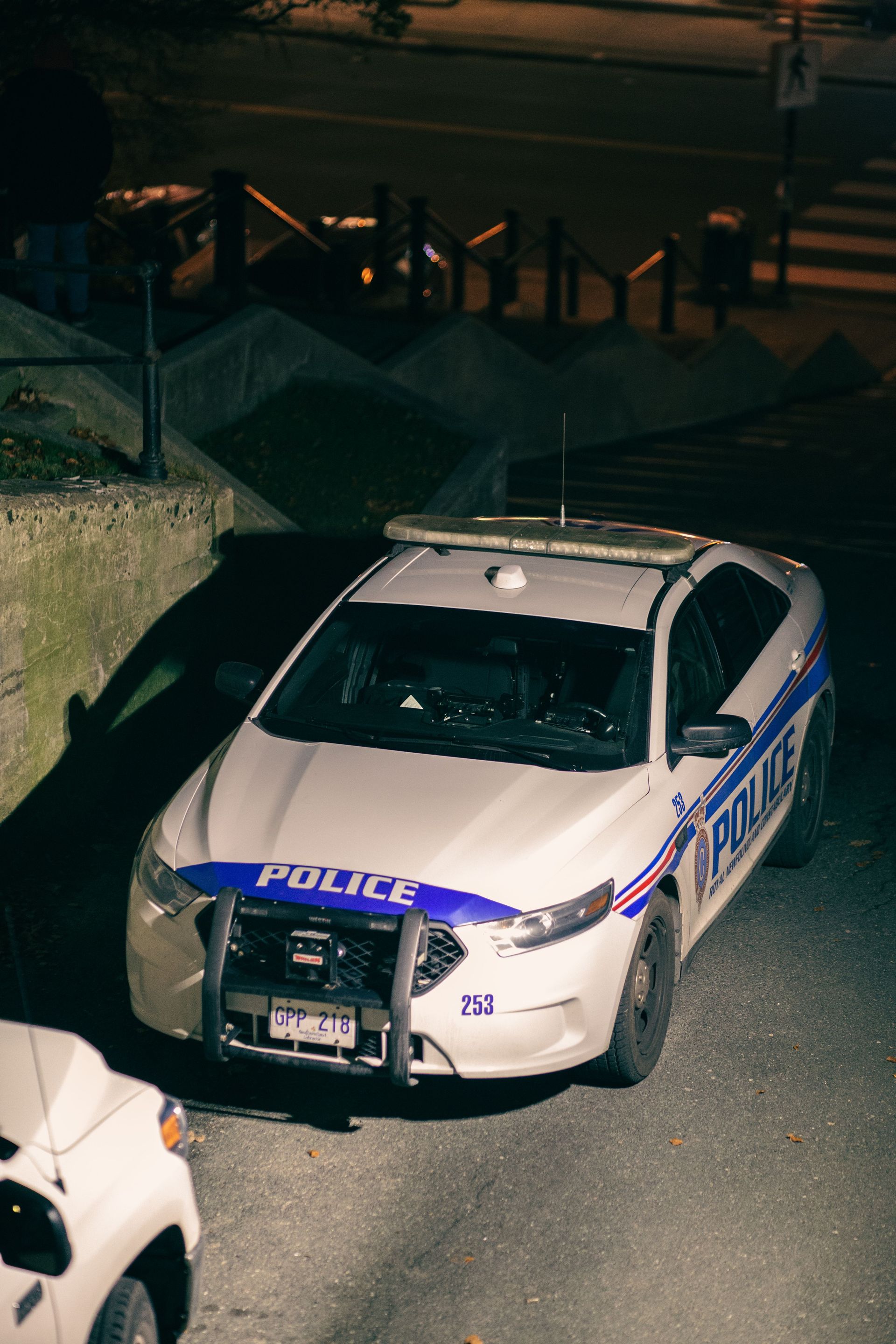 Police car parked on a dimly lit street at night, viewed from above.