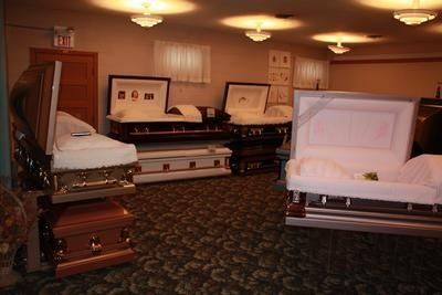 Interior of a funeral home with several open caskets on display, illuminated by overhead lights.