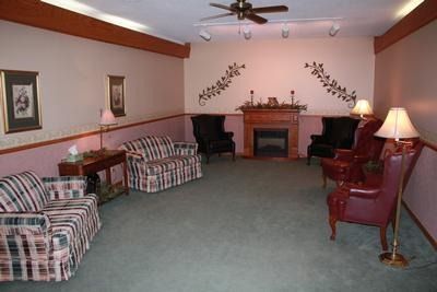 Funeral home waiting area with patterned sofas, armchairs, fireplace, and lamps.