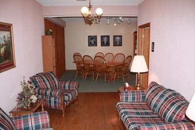 Living room with plaid furniture, opening to a dining area with a long table and portraits.