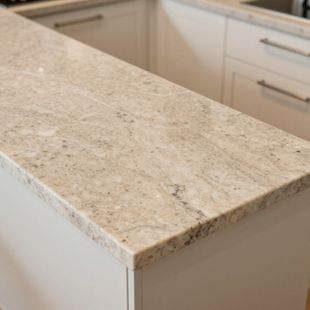 A light-colored granite countertop with speckled cream and grey tones atop white kitchen cabinetry.