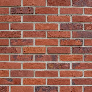 A close-up view of a red brick wall with varying shades of brown and textured surfaces, arranged in a running bond pattern.