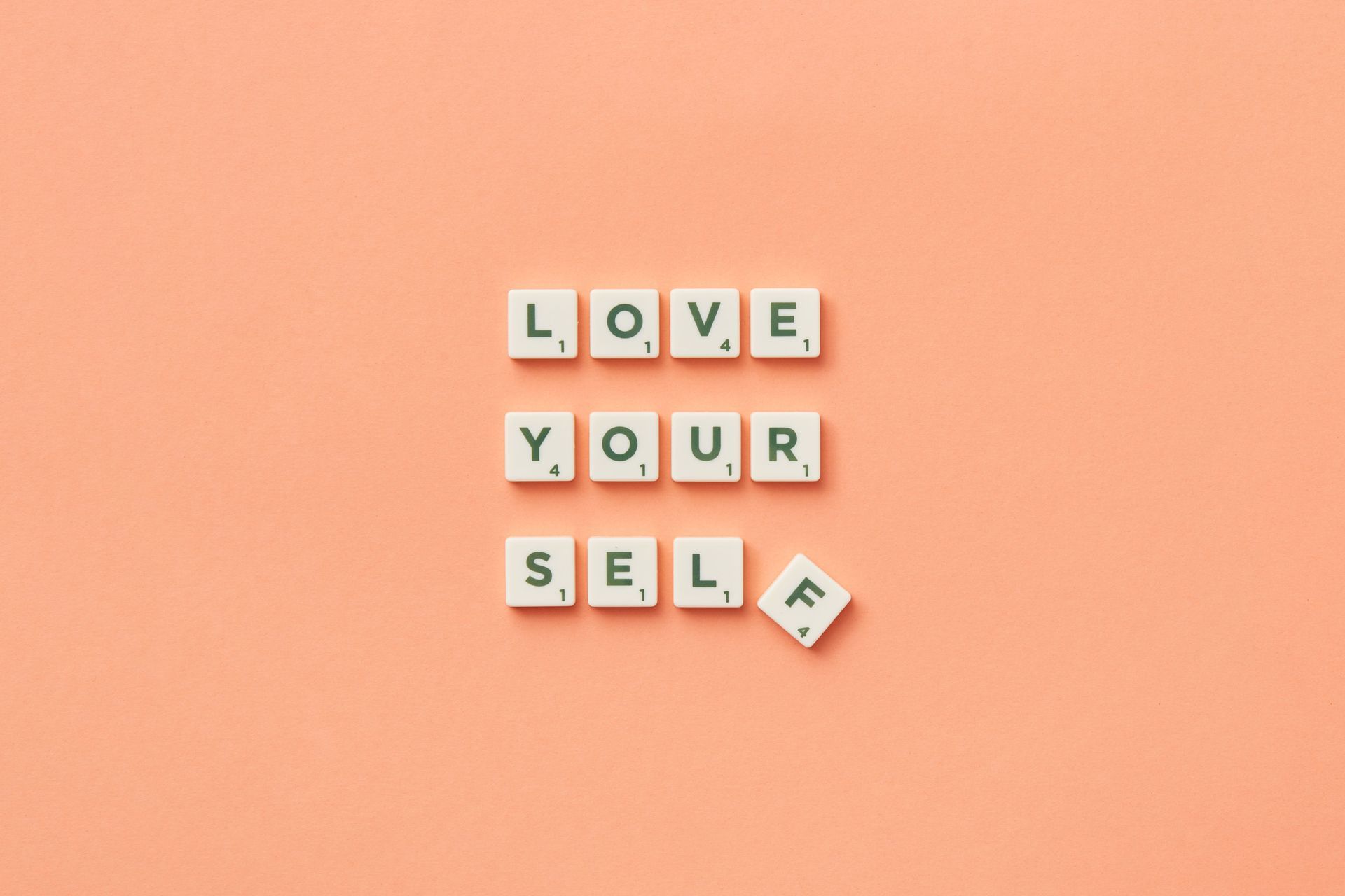 Letter tiles spelling “LOVE YOUR SELF” on a peach background