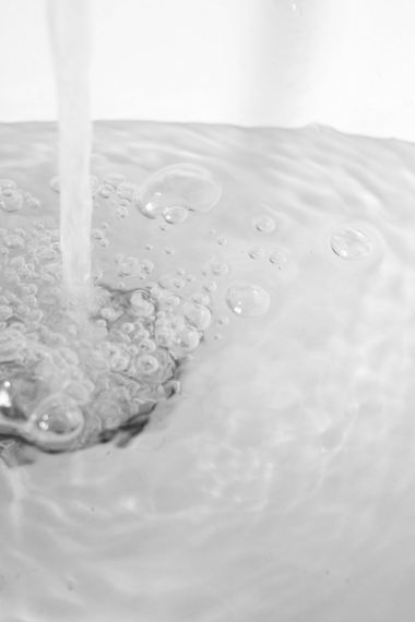 Water pouring into a white sink, creating bubbles and ripples.