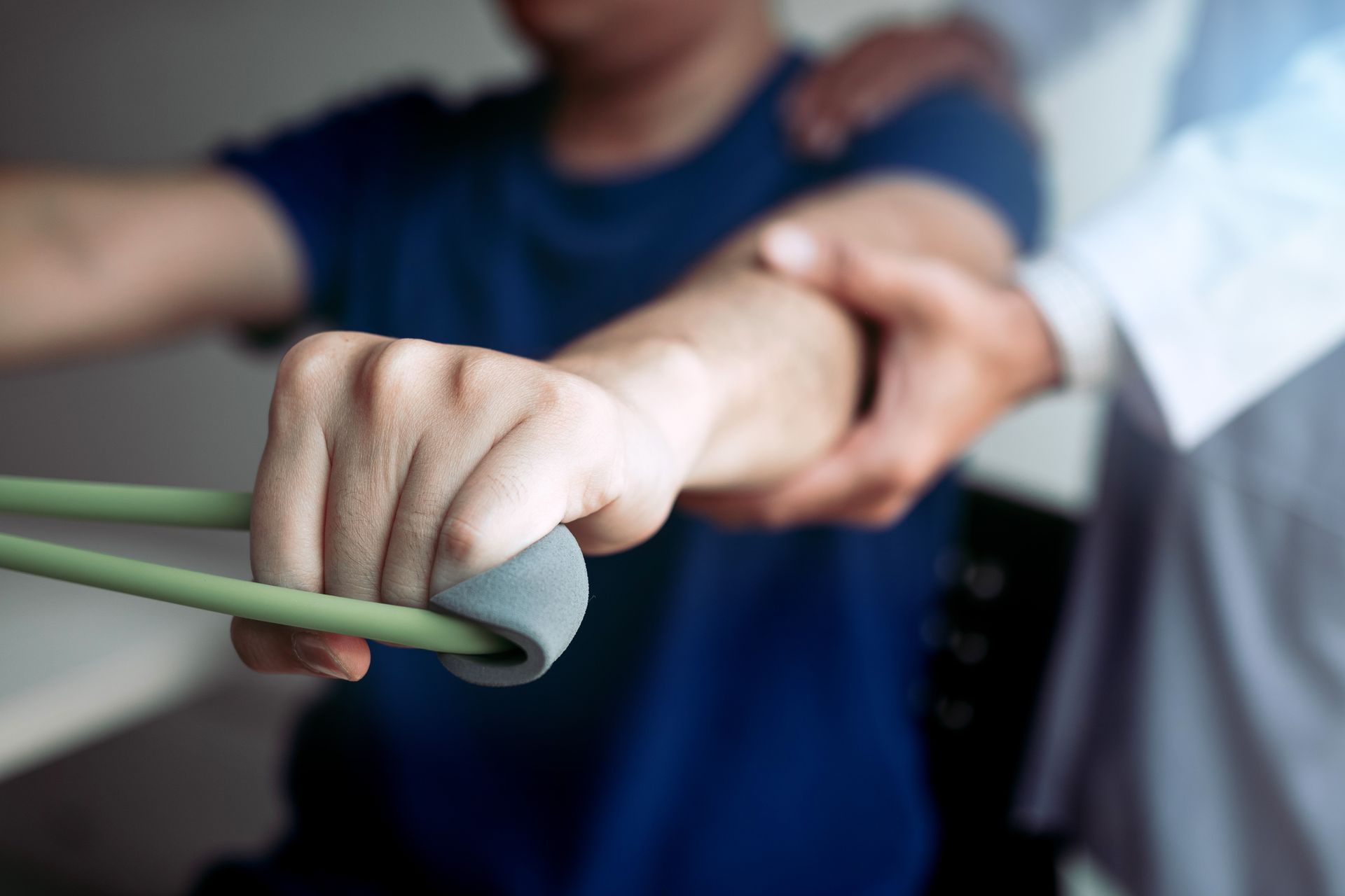 A therapist supports a patient's arm as they use a resistance band for physical therapy exercise.
