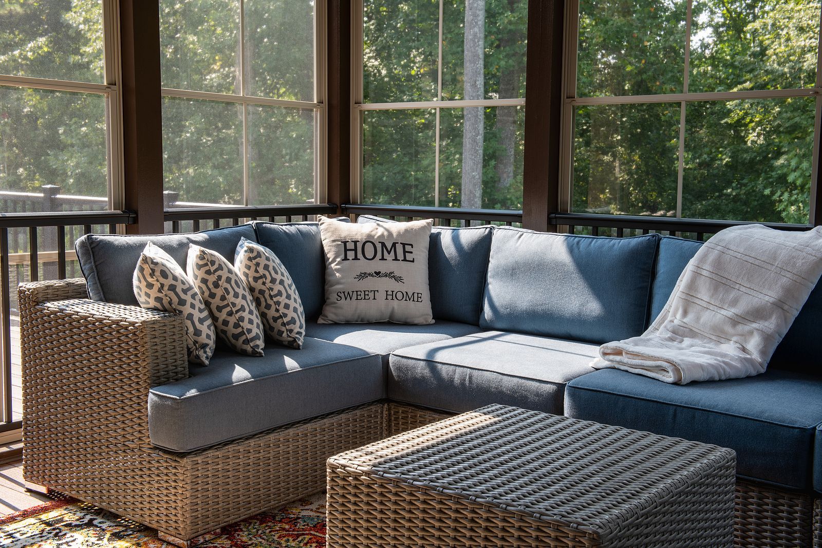 A screened in porch with a sectional couch and a coffee table.