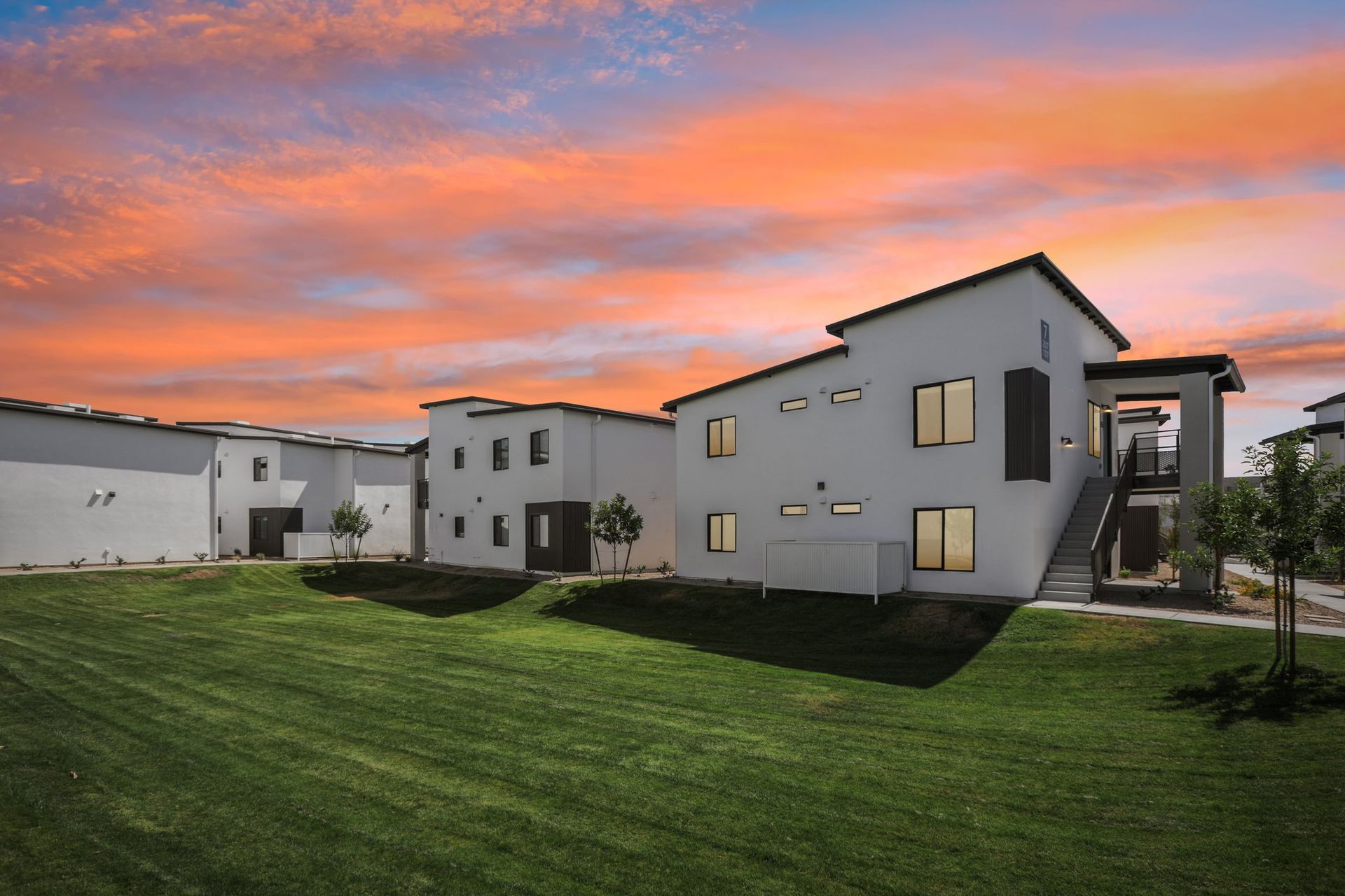 Modern apartment buildings beside a green lawn under a colorful sunset sky