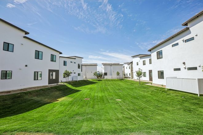 Courtyard between white apartment buildings with a bright green lawn and blue sky