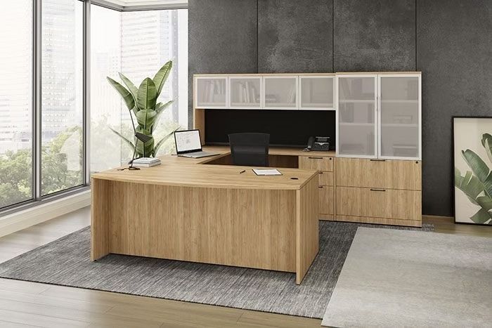 A wooden desk with a laptop on it is in a room with a lot of windows.