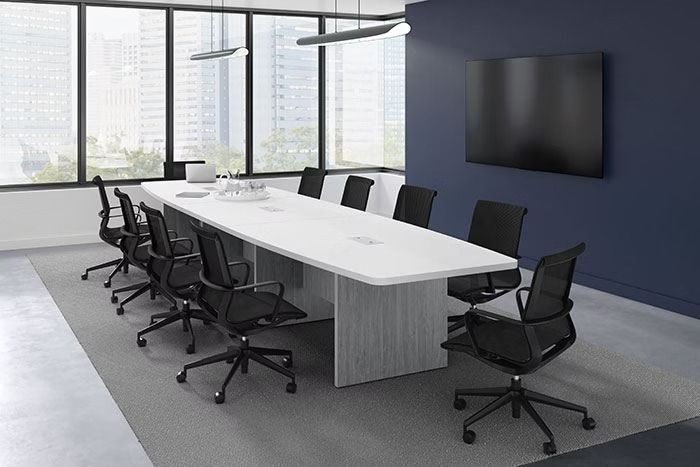 A conference room with a long white table and black chairs.