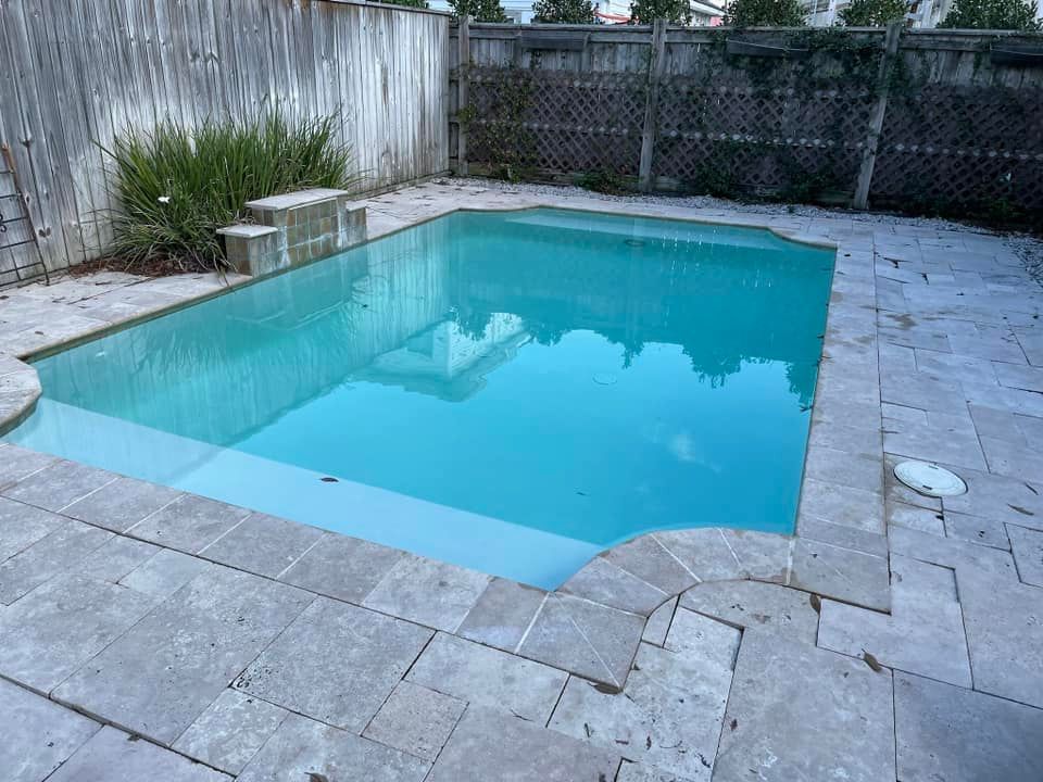Small backyard swimming pool with turquoise water, surrounded by gray pavers and a wooden fence.