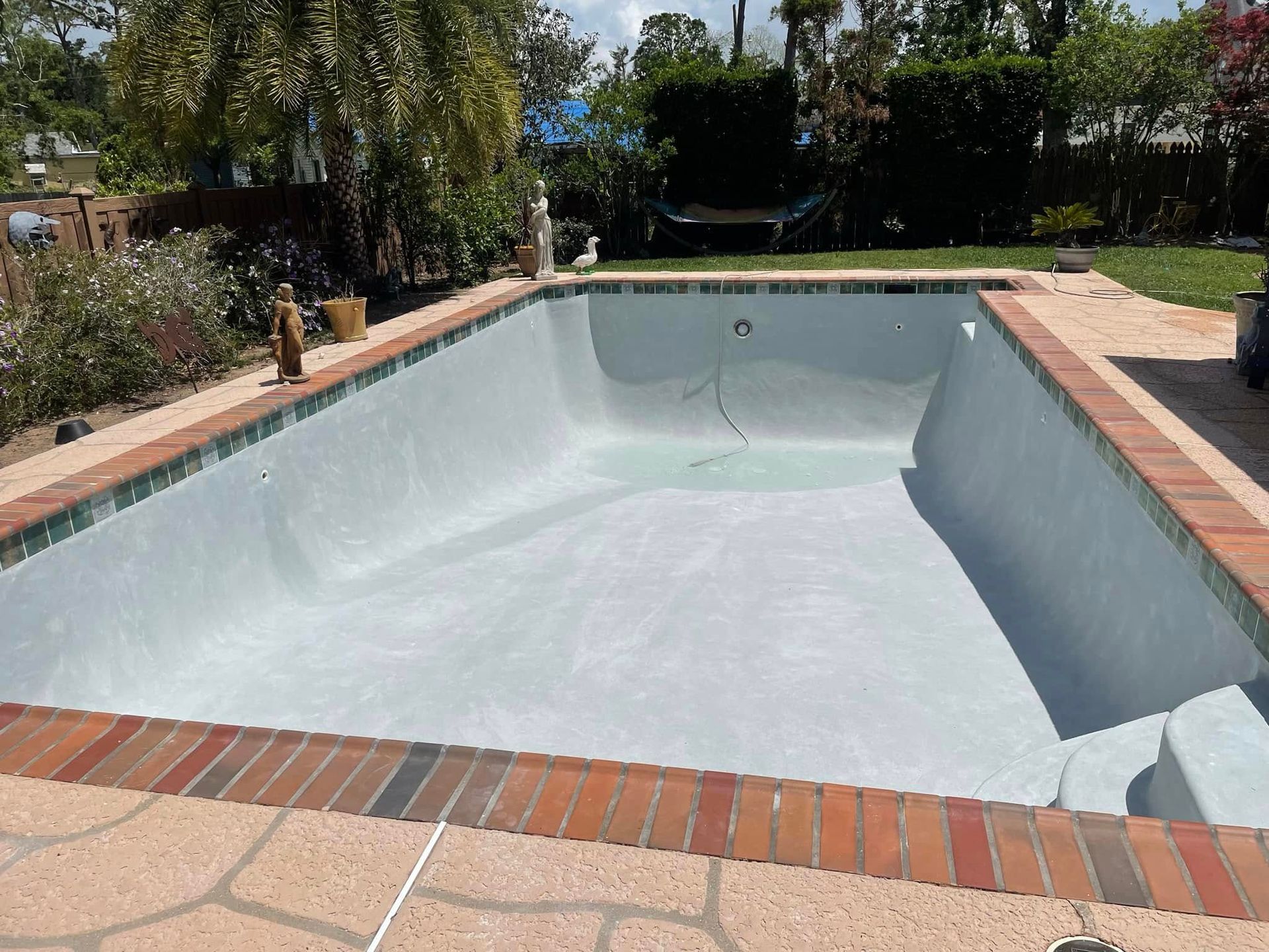Empty swimming pool with white interior and brick coping in a sunny backyard garden