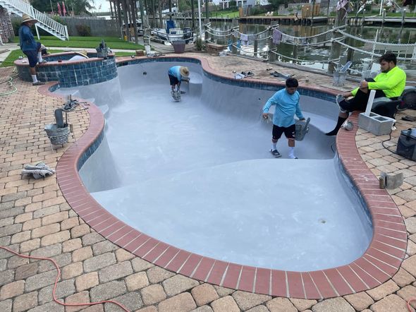 People skate in a drained pool at a brick-lined park.
