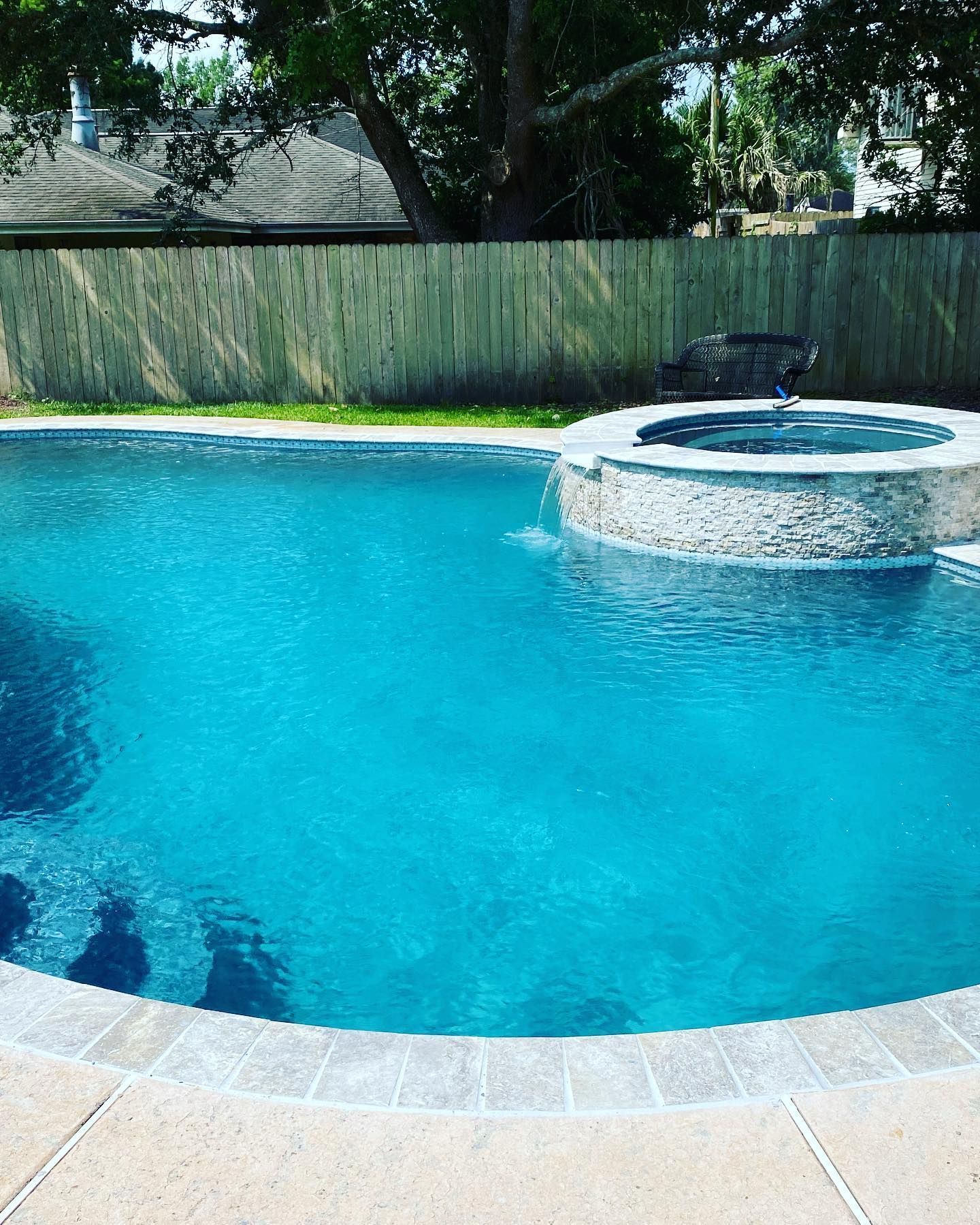 Blue backyard swimming pool with a raised circular hot tub and wooden fence backdrop