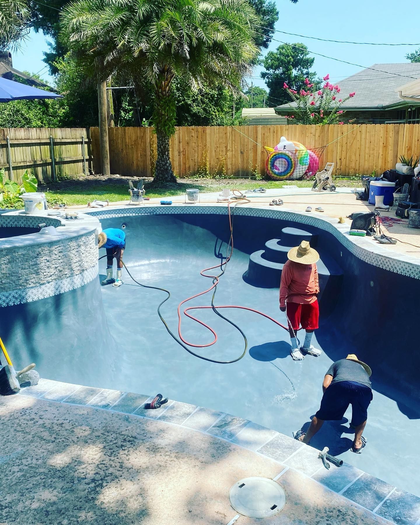 Children playing in an empty backyard pool with hoses and pool-cleaning gear on a sunny day