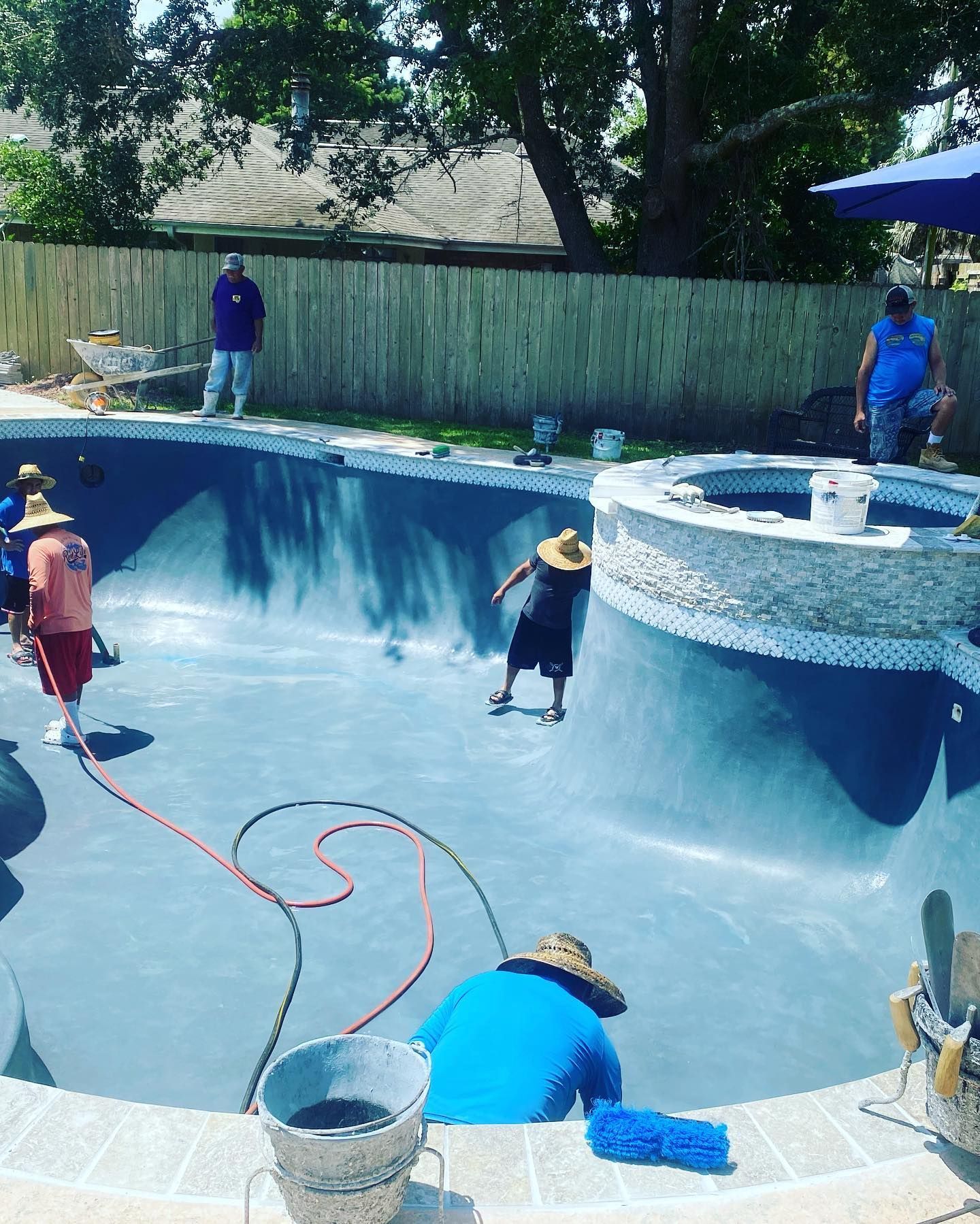 Pool being cleaned by workers using hoses and buckets, with one person leaning over the pool edge.