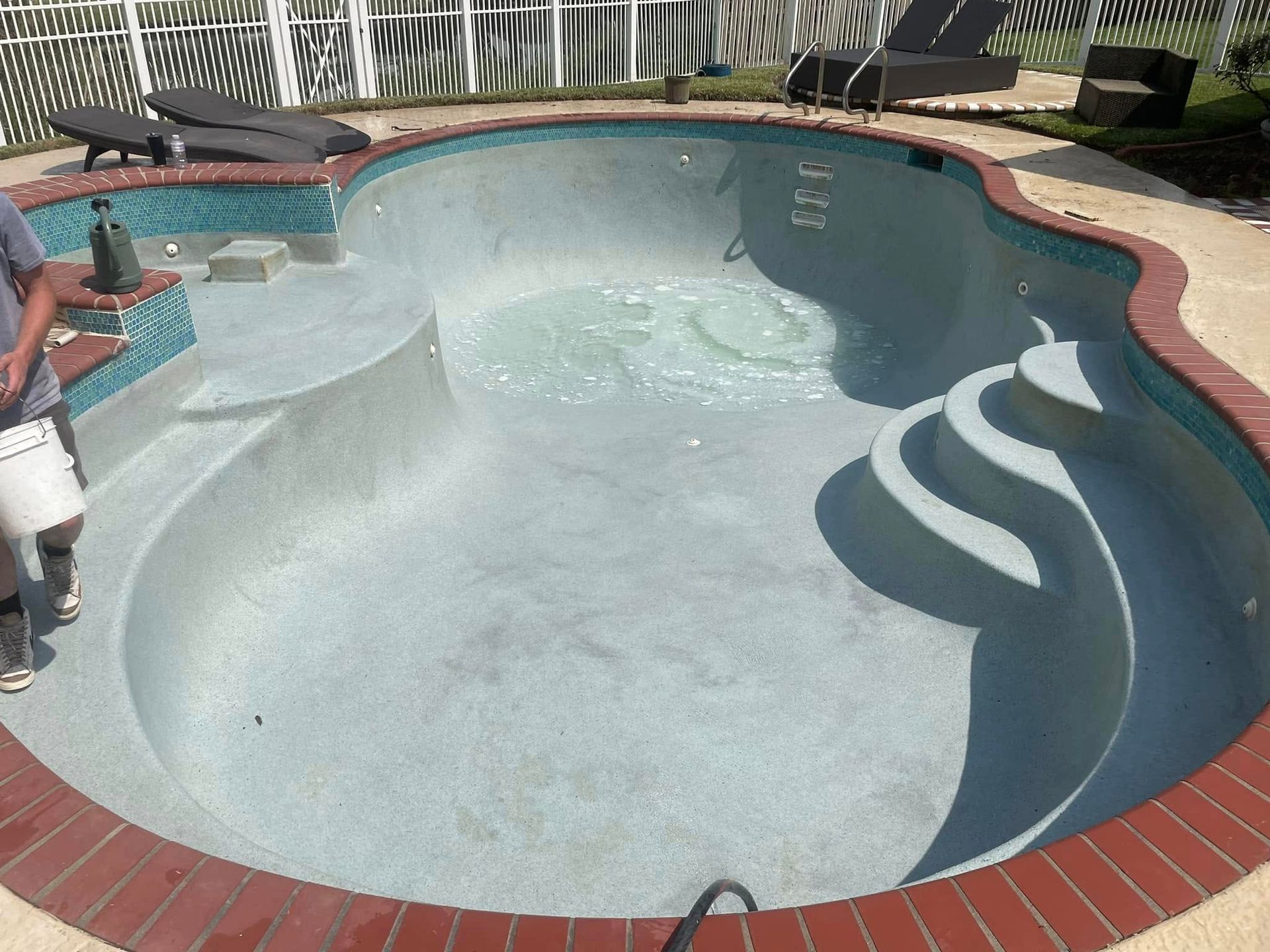 Empty backyard swimming pool with blue interior, red brick border, and curved steps