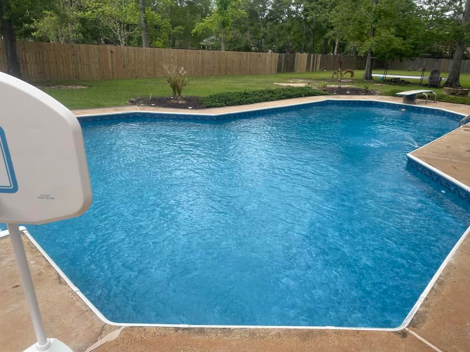 Backyard swimming pool with blue water, concrete deck, basketball hoop, and fenced green lawn.