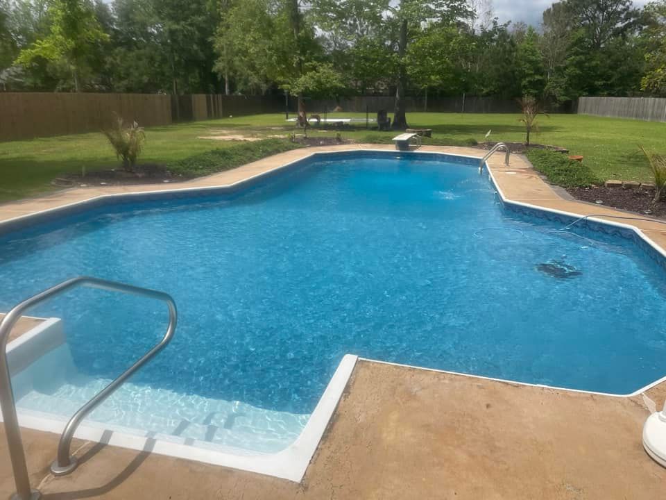 Backyard swimming pool with blue water, tan deck, and green lawn on a sunny day