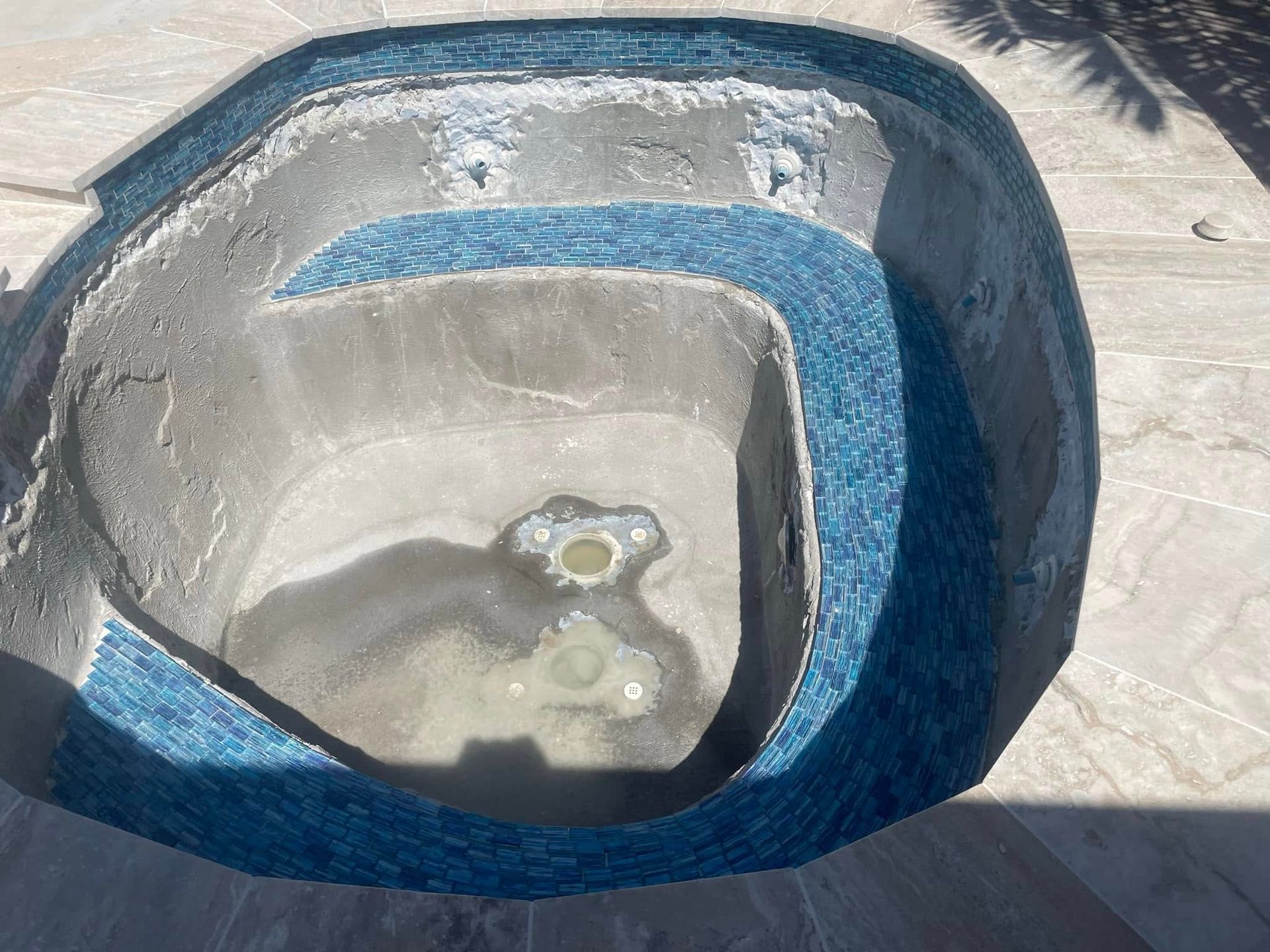 Empty concrete basin with blue-tiled rim and small puddle of water.