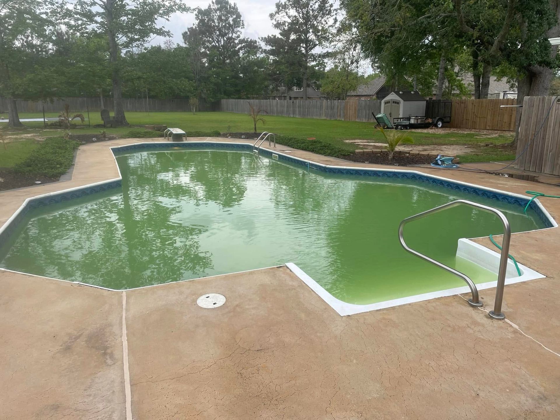 Backyard swimming pool with green water and a metal handrail on a concrete deck