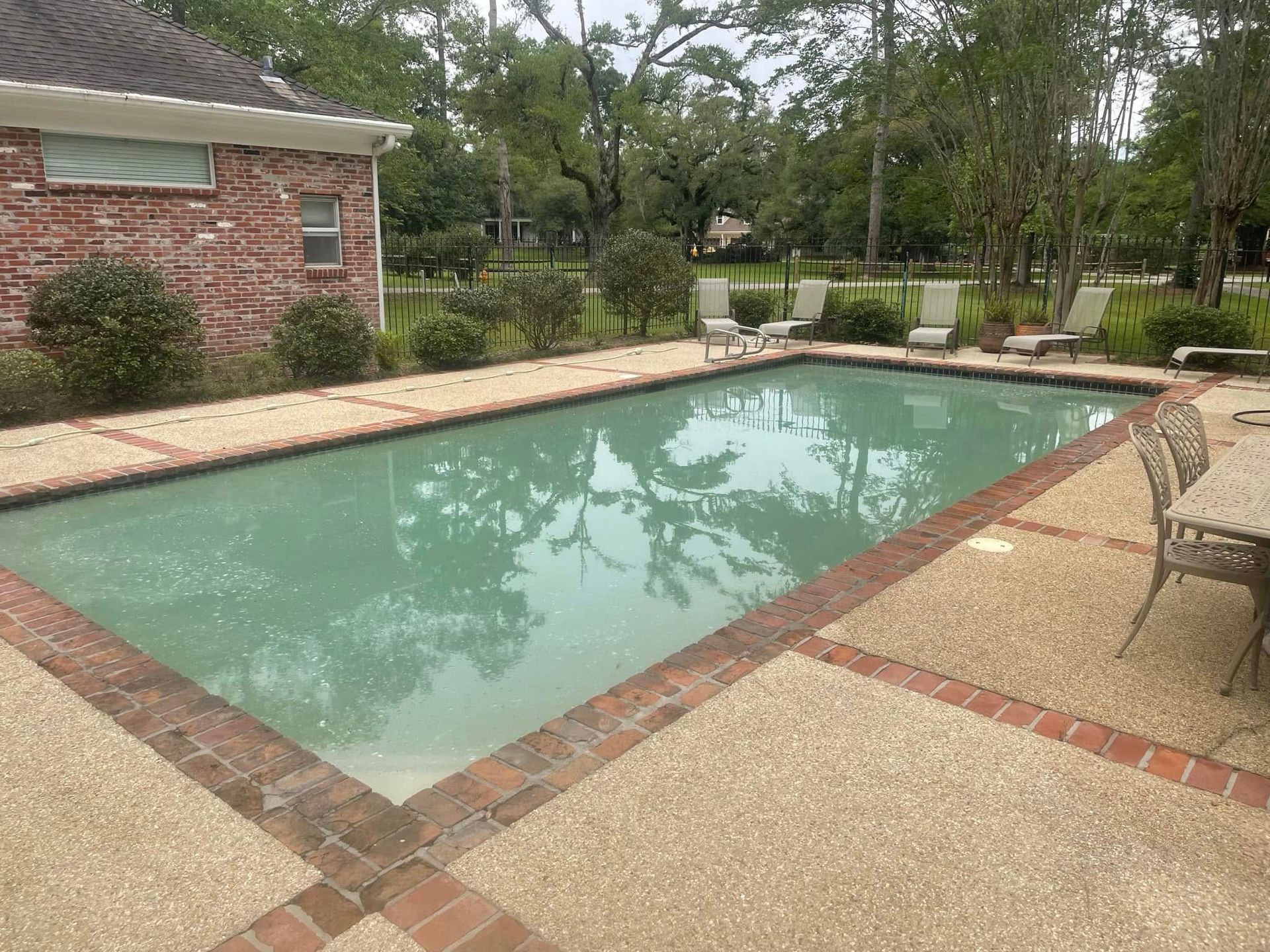 Backyard swimming pool with brick patio, lounge chairs, and trees