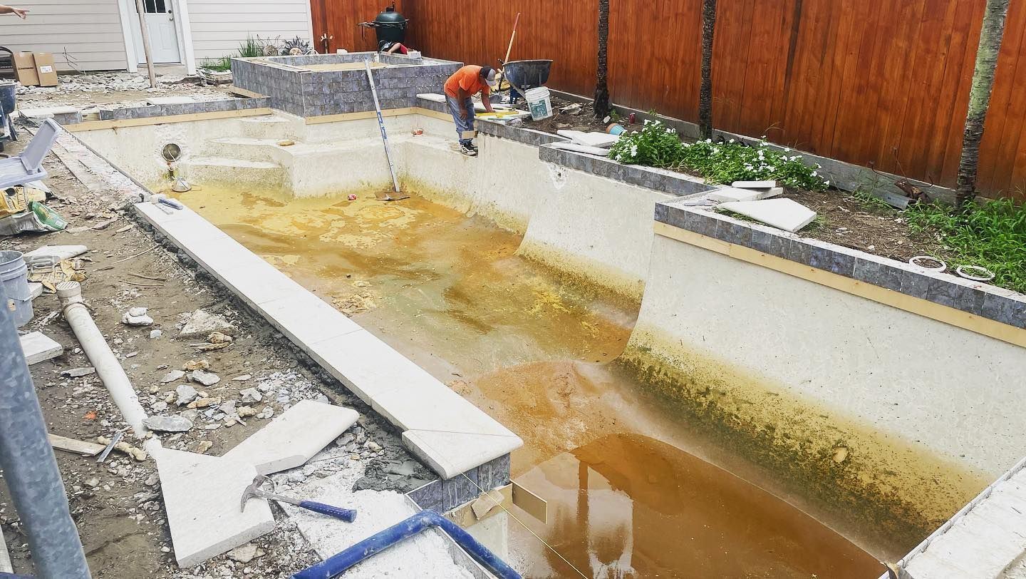Partially built concrete pool or water feature with muddy water and workers on site