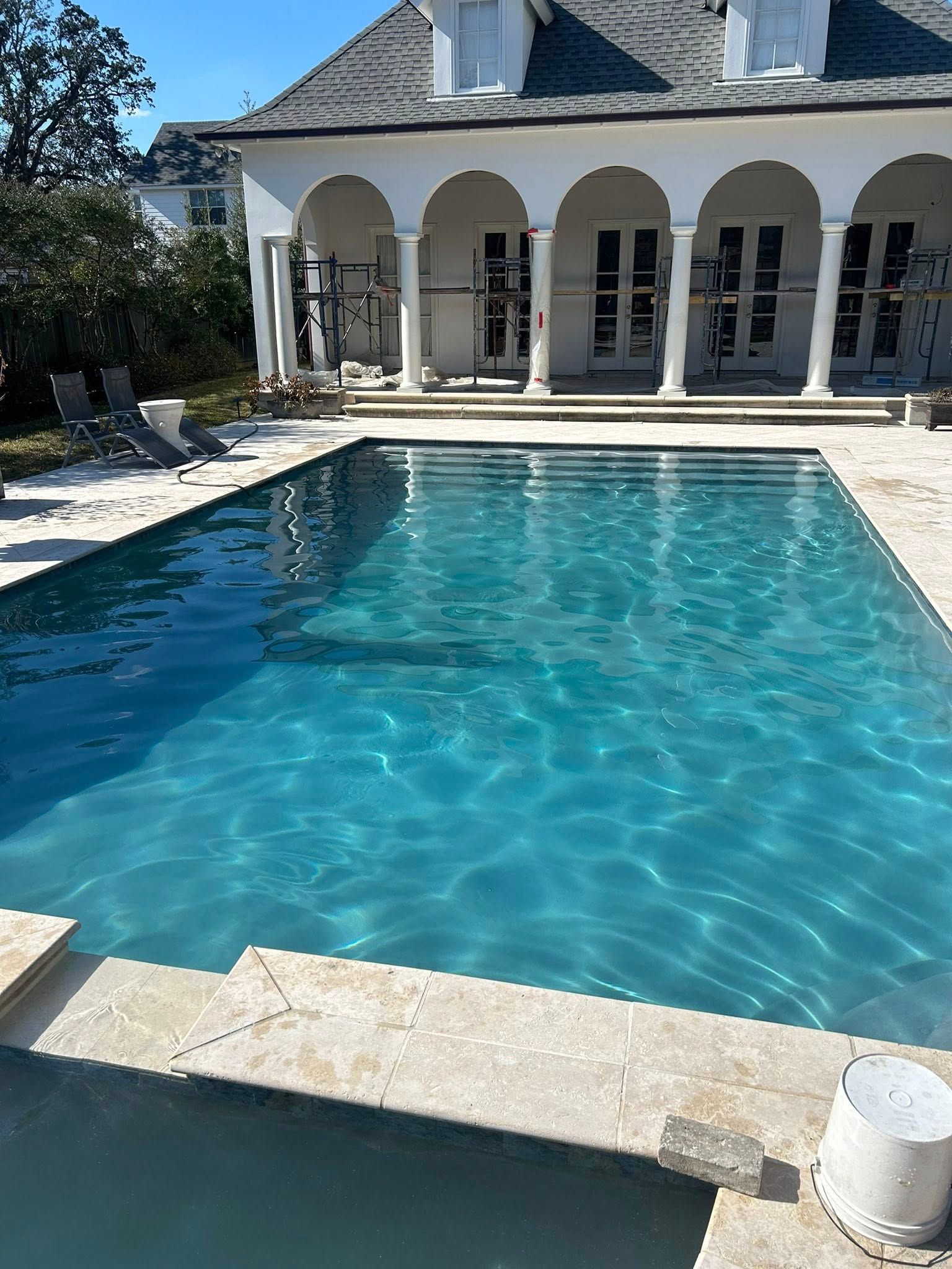 Blue swimming pool beside a white arched villa under bright sunlight