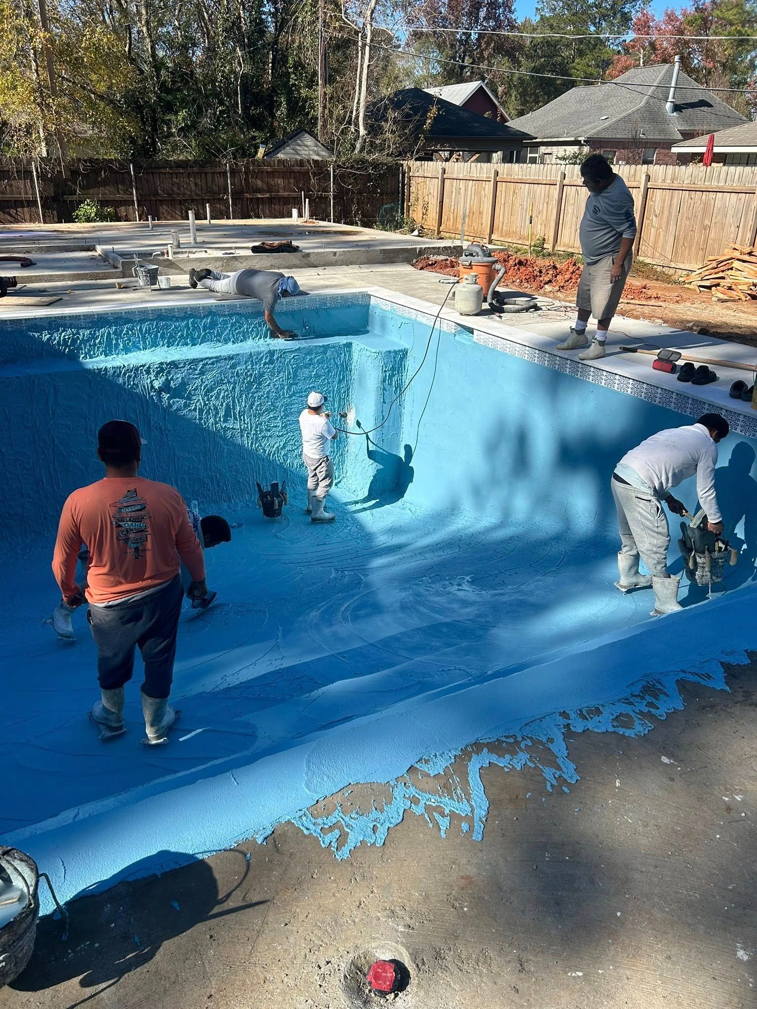 Workers painting a drained pool bright blue, with one person inside and others around the edge.