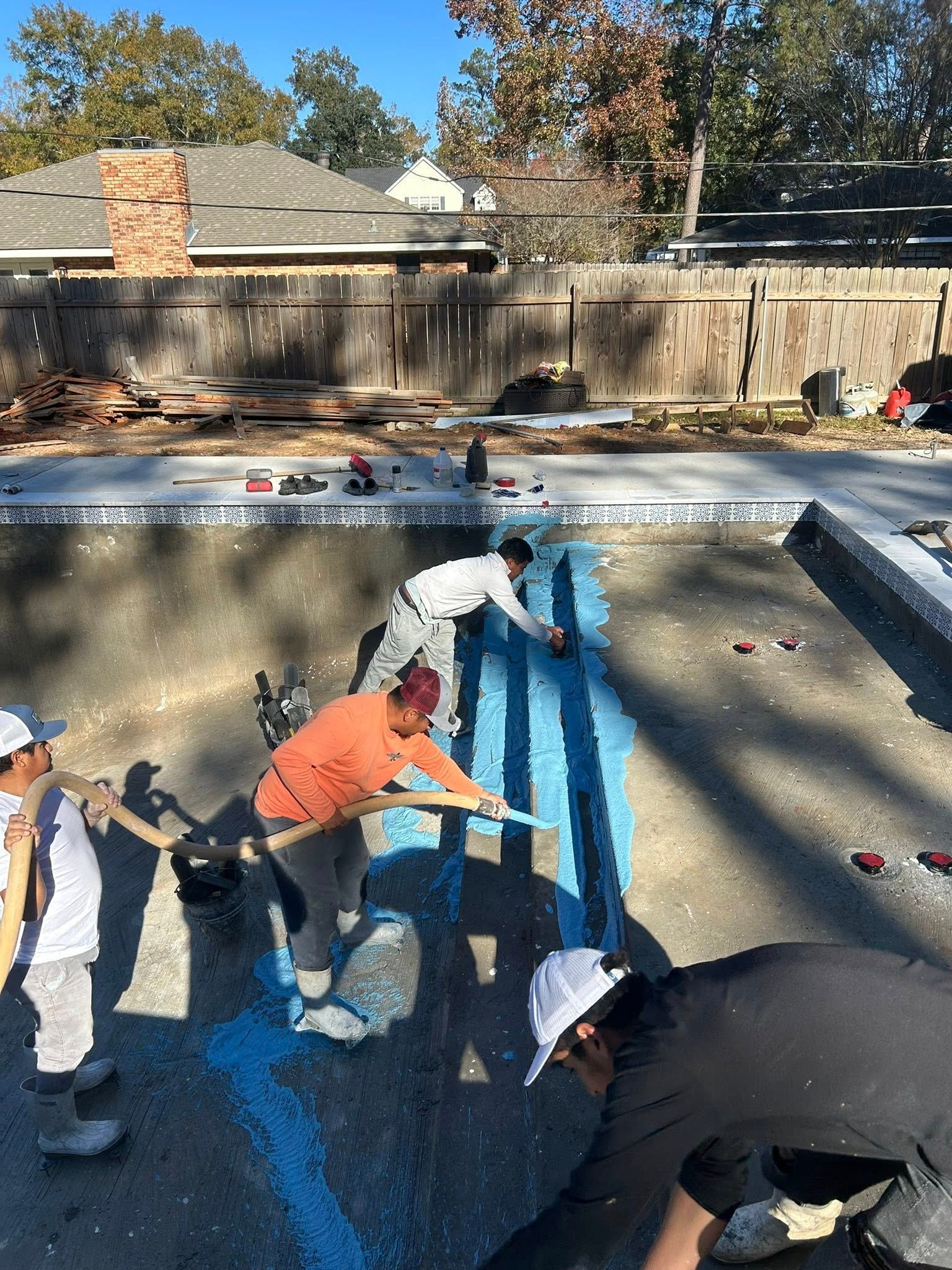 People scraping and painting a blue-lined pool at a backyard house.