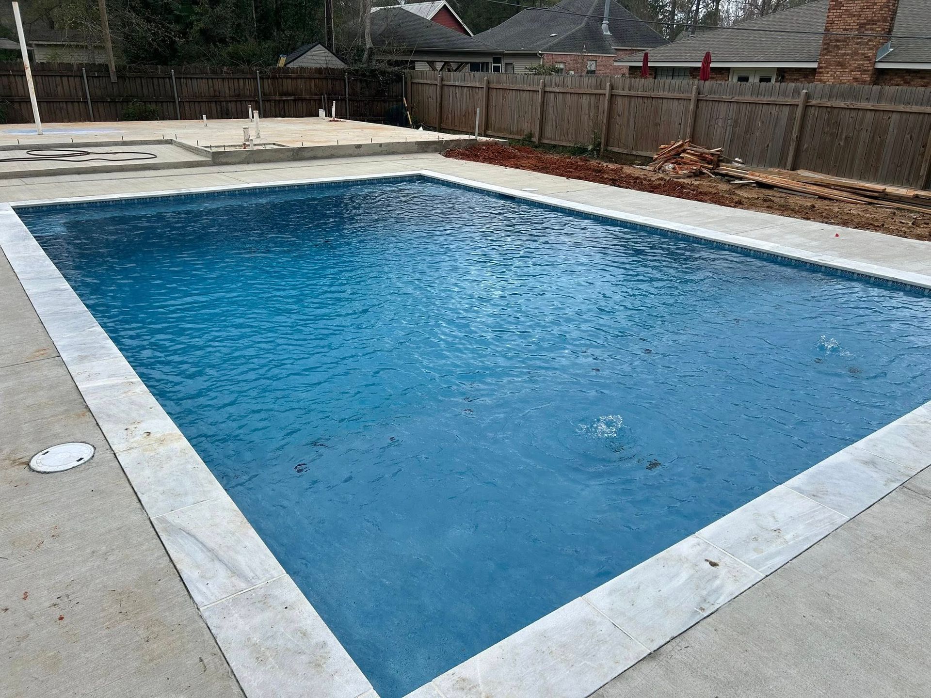 Rectangular outdoor swimming pool with blue water and a light stone deck in a backyard setting