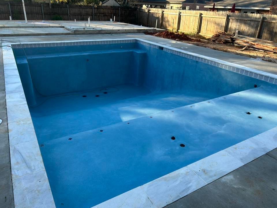 Empty blue swimming pool under construction with concrete deck and surrounding fence
