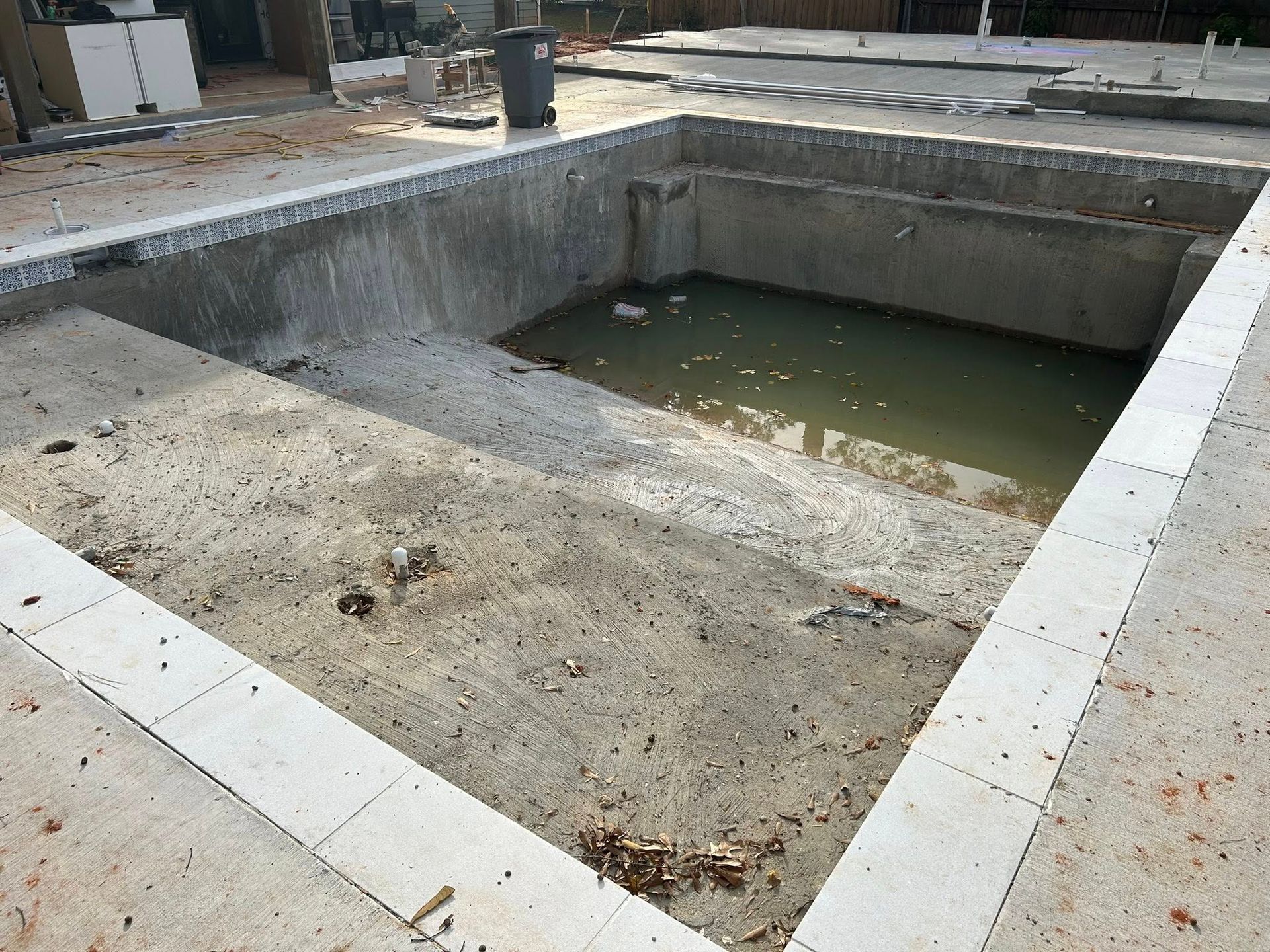 Concrete empty pool basin with muddy water at the bottom, viewed from above in an outdoor construction area