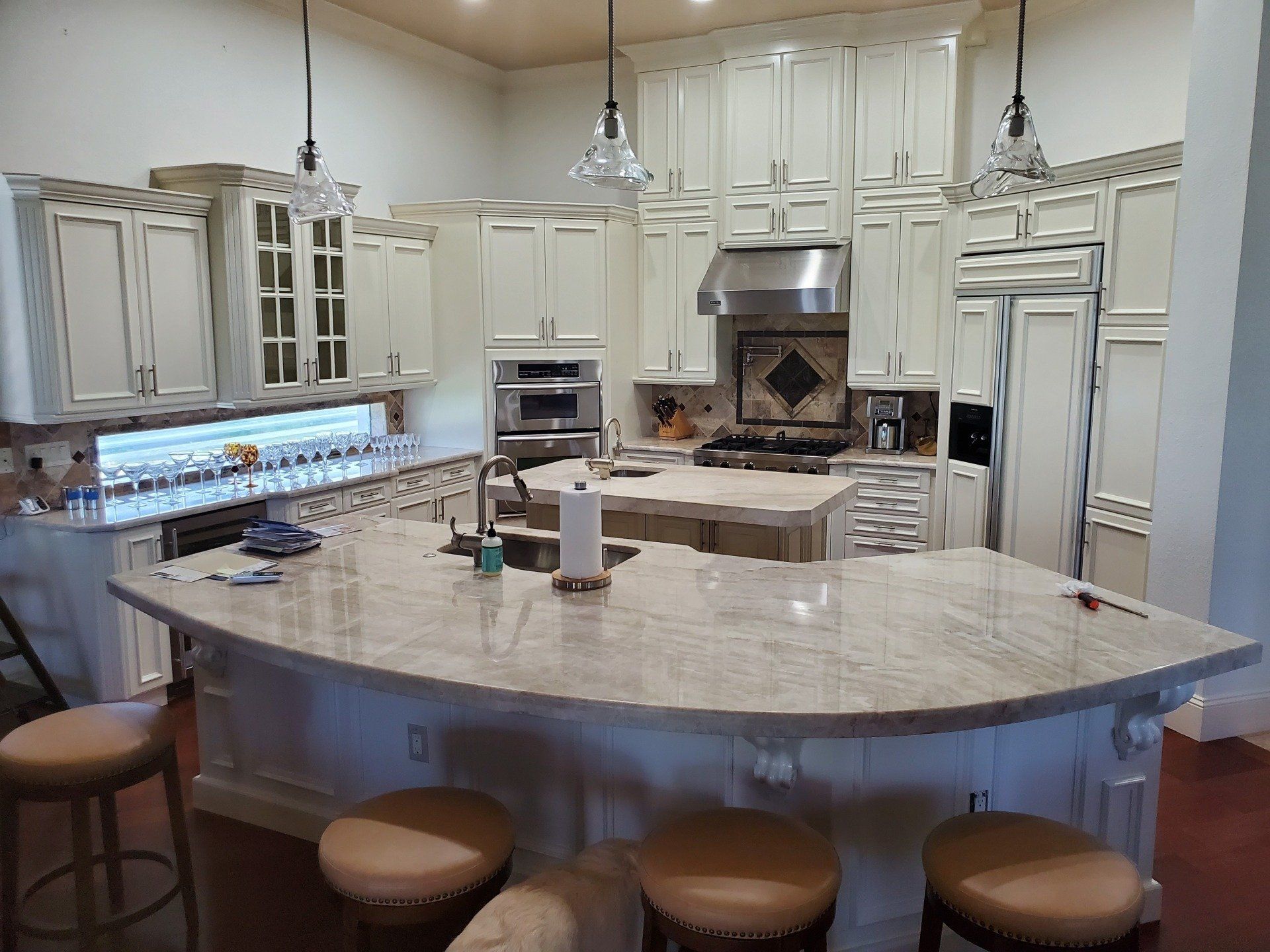 Cream-colored kitchen with granite countertops, island, and bar stools; stainless steel appliances.