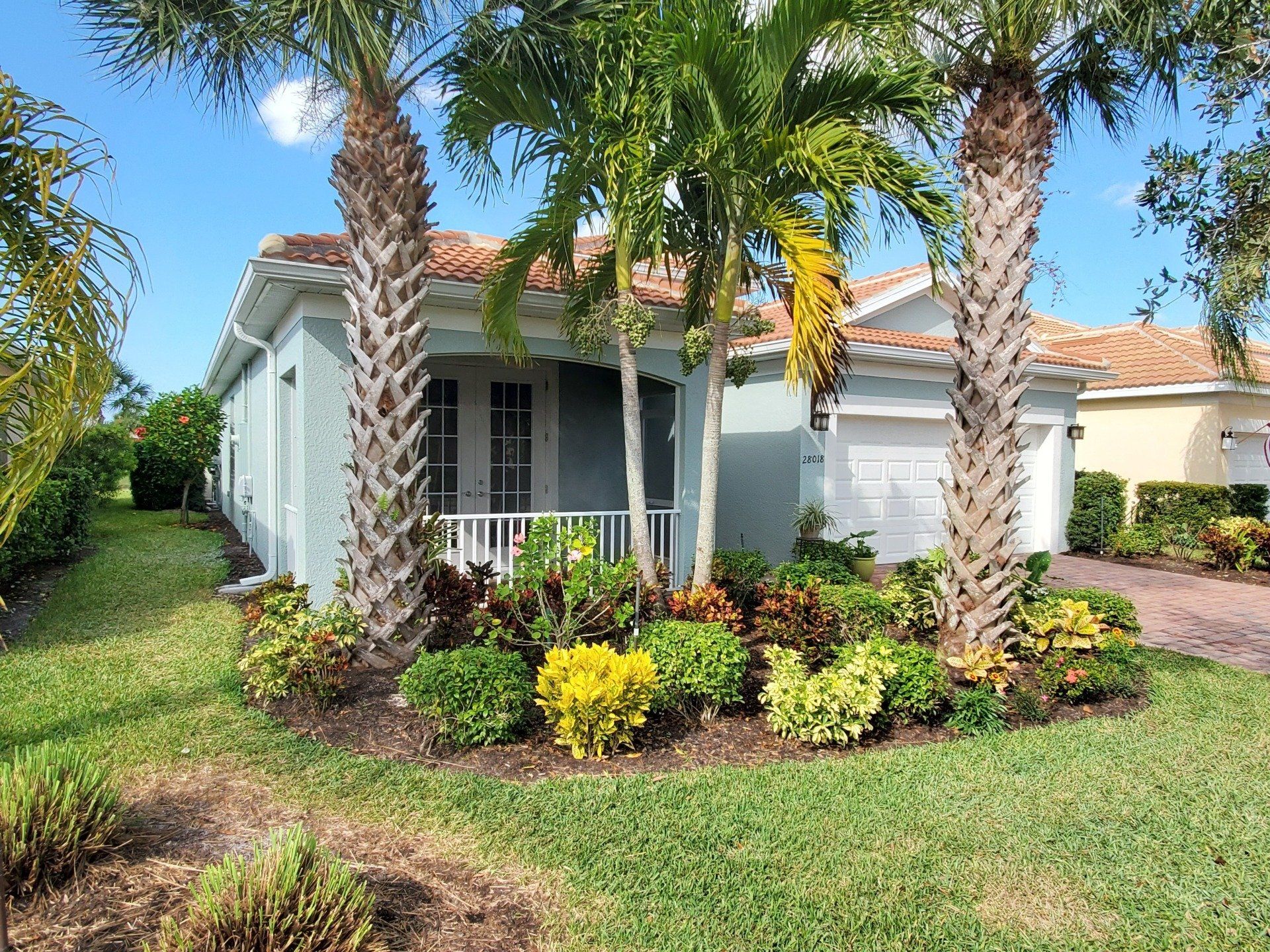 Blue house with palm trees and colorful landscaping on a sunny day.