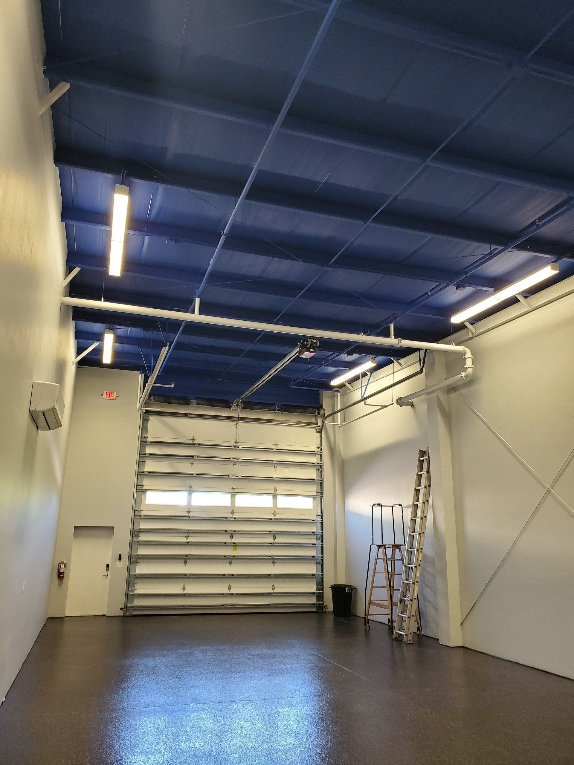 Open garage interior with blue ceiling, white walls, open garage door, and ladder.