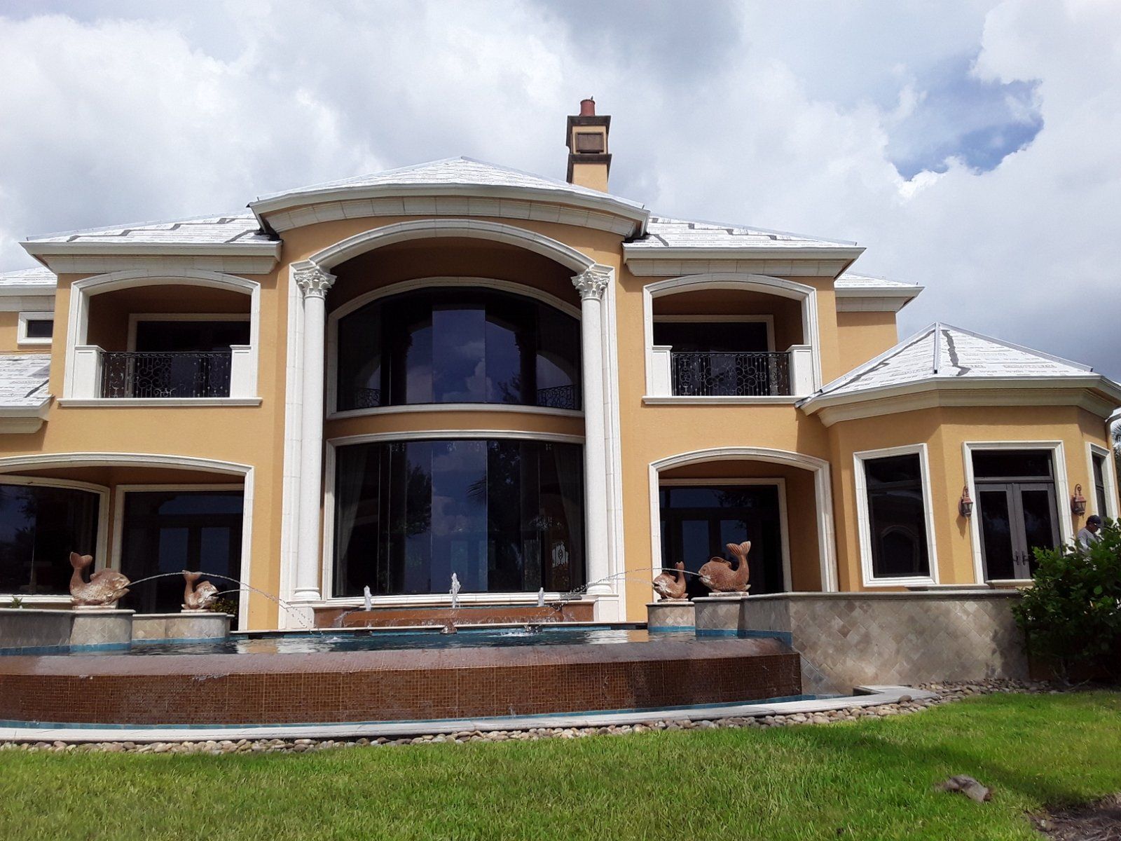 Luxurious tan mansion with white accents, large windows, and a pool.