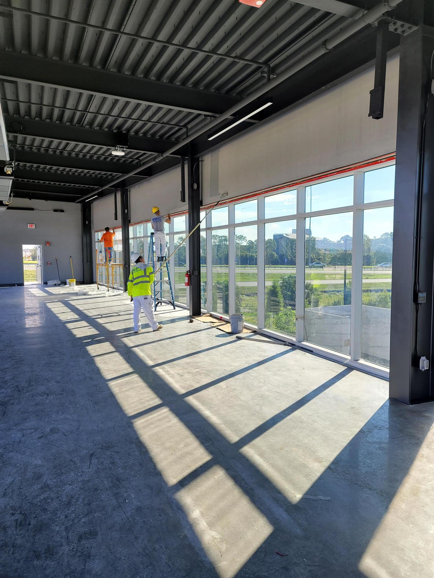 Construction workers inside a new building, working on windows, with concrete floors and metal framing.