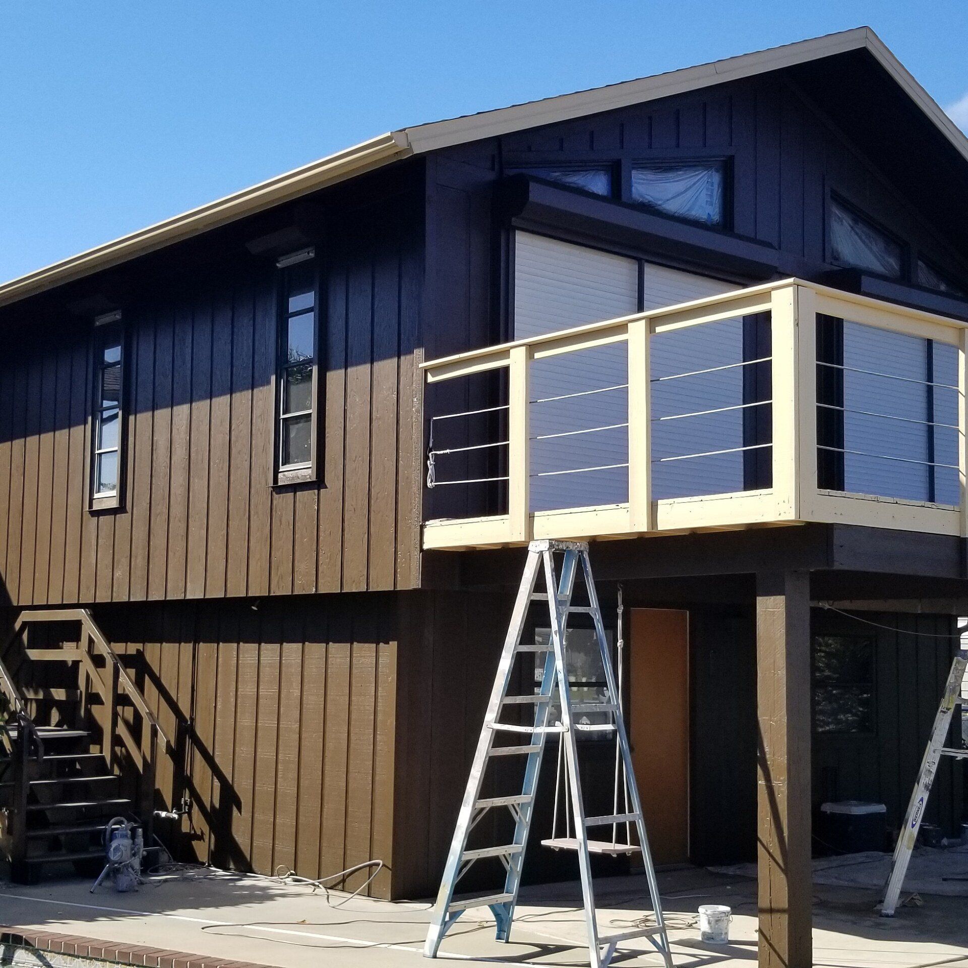 Brown house with cream trim, ladder in front of a balcony, and clear blue sky.