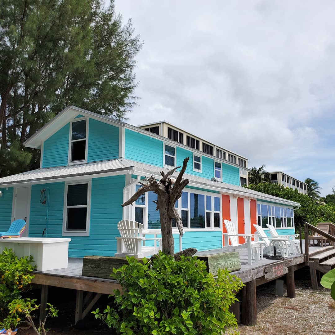 Colorful beachfront cottage with turquoise and orange siding, white trim, and deck with chairs.